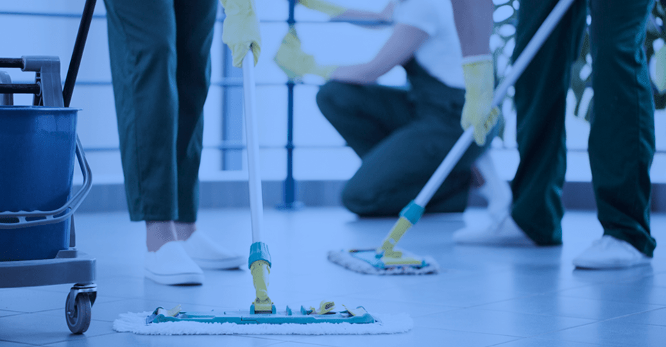 Facilities Macor - Imagem de agentes de limpeza encerando o chão com esfregões.