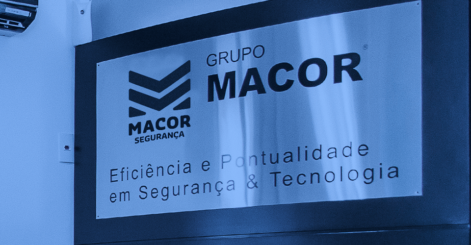 Nossa História - imagem de painel de metal, no topo de totem, com o logo do grupo Macor e os escritos: Eficiência e Pontualidade em Segurança e Tecnologia.